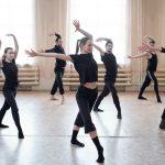 Un groupe de sept danseurs de danse contemporaine, vêtus de noir, exécutent une chorégraphie expressive et dynamique sur le parquet d'un studio lumineux au sein de notre centre de danse